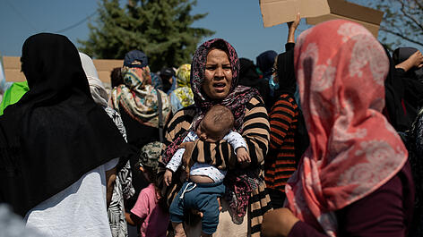 A woman holds a baby as refugees and migrants from the destroyed Moria camp protest near a new temporary camp, on the island of Lesbos