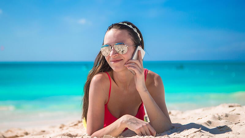 Young woman lying on white sand and talking by her phone,smartphone handy strand beach roaming