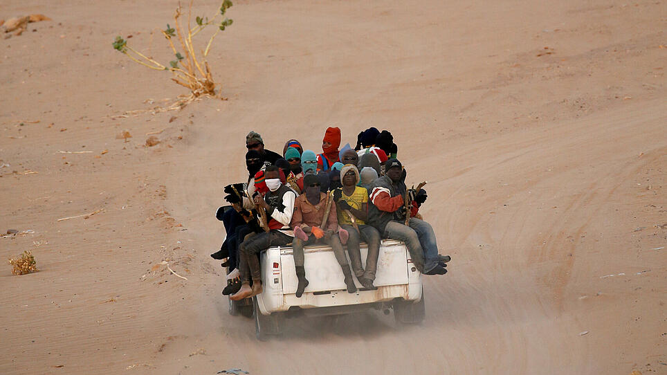 FILE PHOTO: Migrants crossing the Sahara desert into Libya ride on the back of a pickup truck outside Agadez