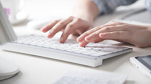 Hands typing on computer keyboard in office desk.