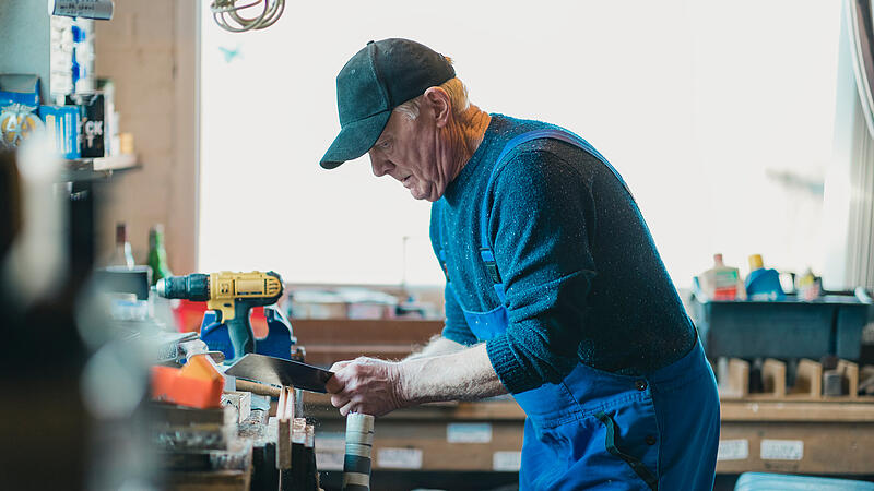 Senior Man Sawing Wood in a Workshop
