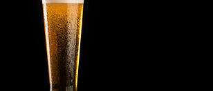 Glass of beer with foam on black background