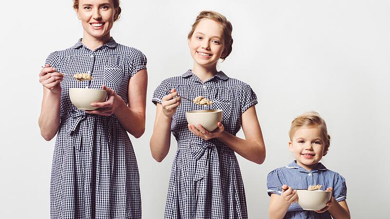 mother and daughters in similar dresses with cereal breakfast in bowls on white