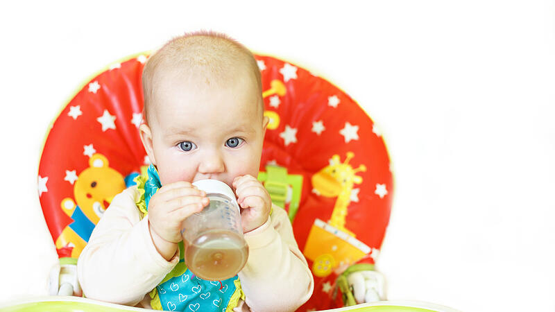 baby drinking from bottle sitting in high chair on a white background