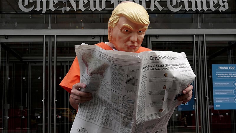 Mike Hisey dressed as U.S. President Donald Trump in a prison jumpsuit reads the New York Times in front of the New York Times