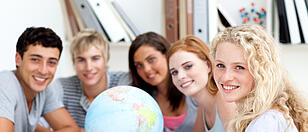 Smiling teenagers in a library working with a terrestrial globe