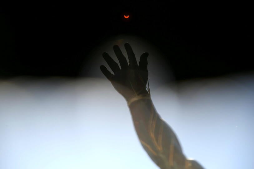 A solar eclipse is seen through filters from special solar glasses in front of a sculpture, in Santiago