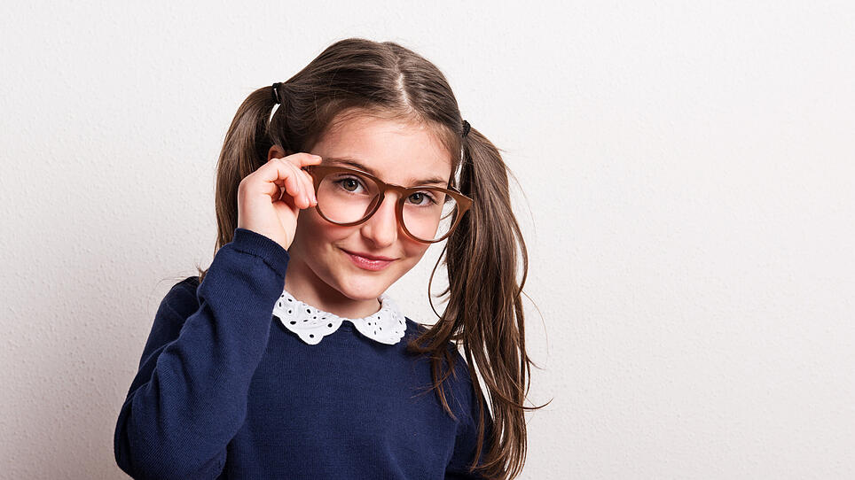 A small cheeky schoolgirl with glasses and uniform in a studio.