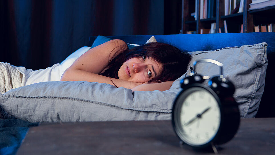Portrait of dissatisfied woman with insomnia lying on bed next to alarm clock at night
