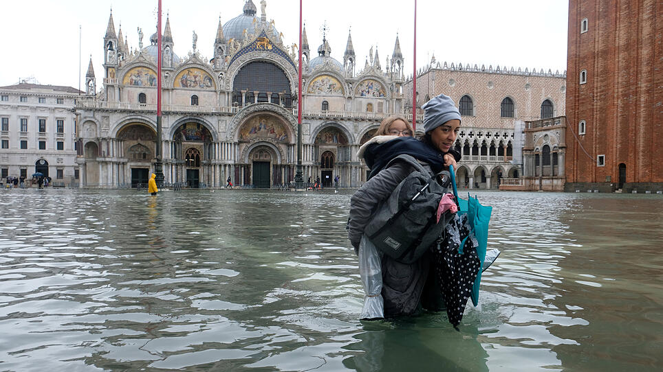 FILE PHOTO: A woman carrying a child on her back wades in the flooded St. Mark's Square in Venice, Italy