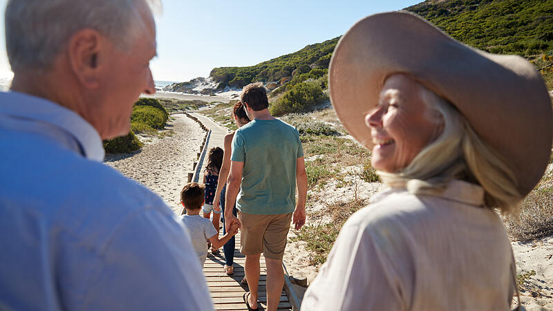 Three generation white family walking on a beach, grandparents in the foreground, over shoulder view