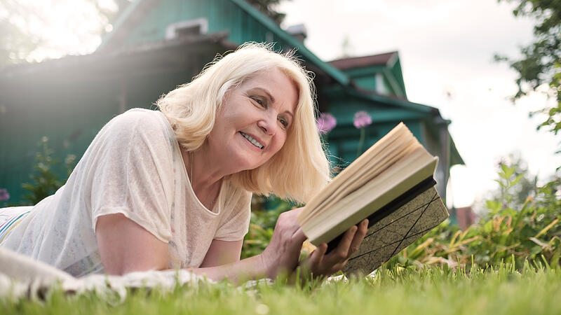 European mature blonde woman reading a book in the garden.